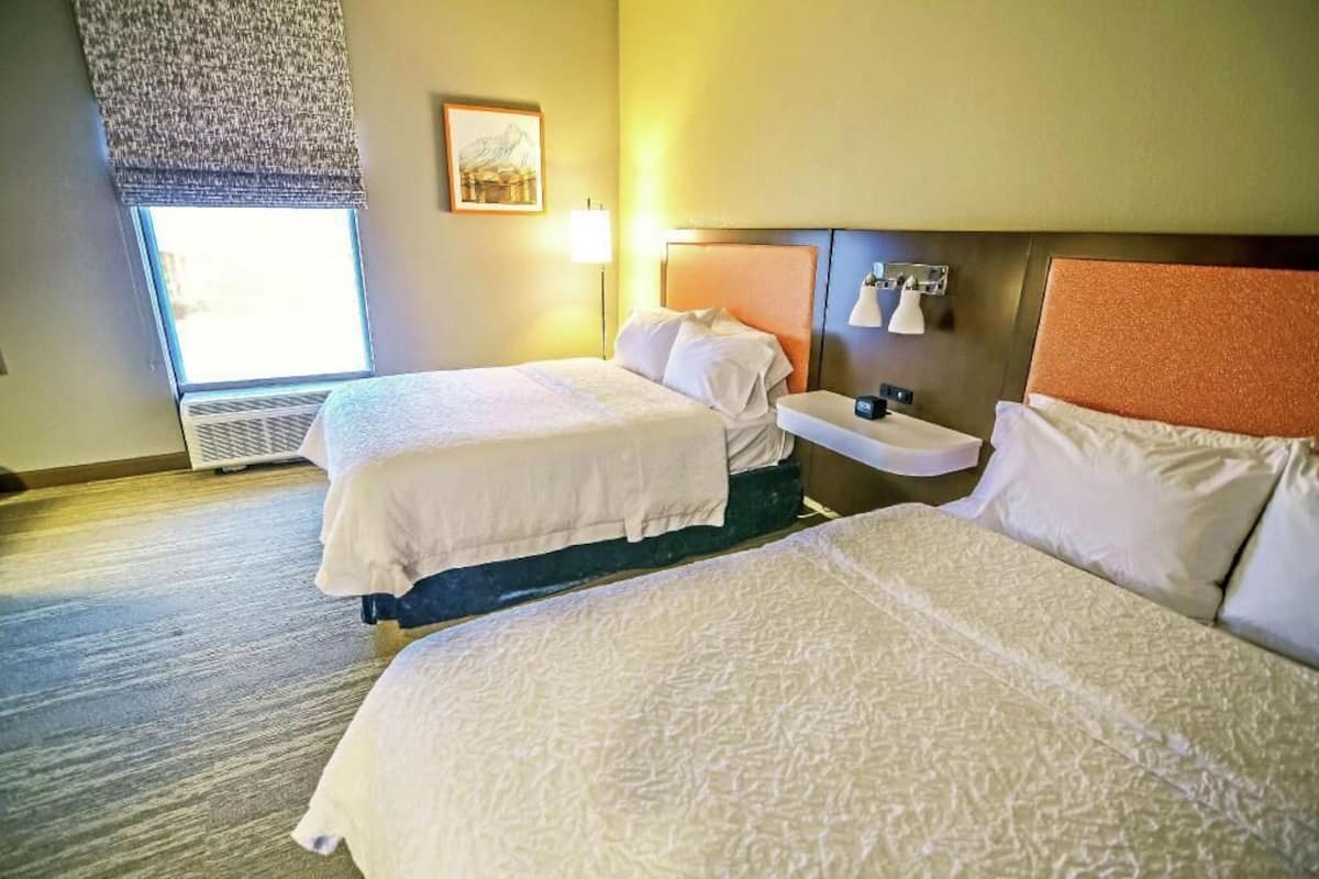 Une chambre d’hôtel avec deux lits, une table de chevet, une lampe et une fenêtre donnant sur un beau paysage.