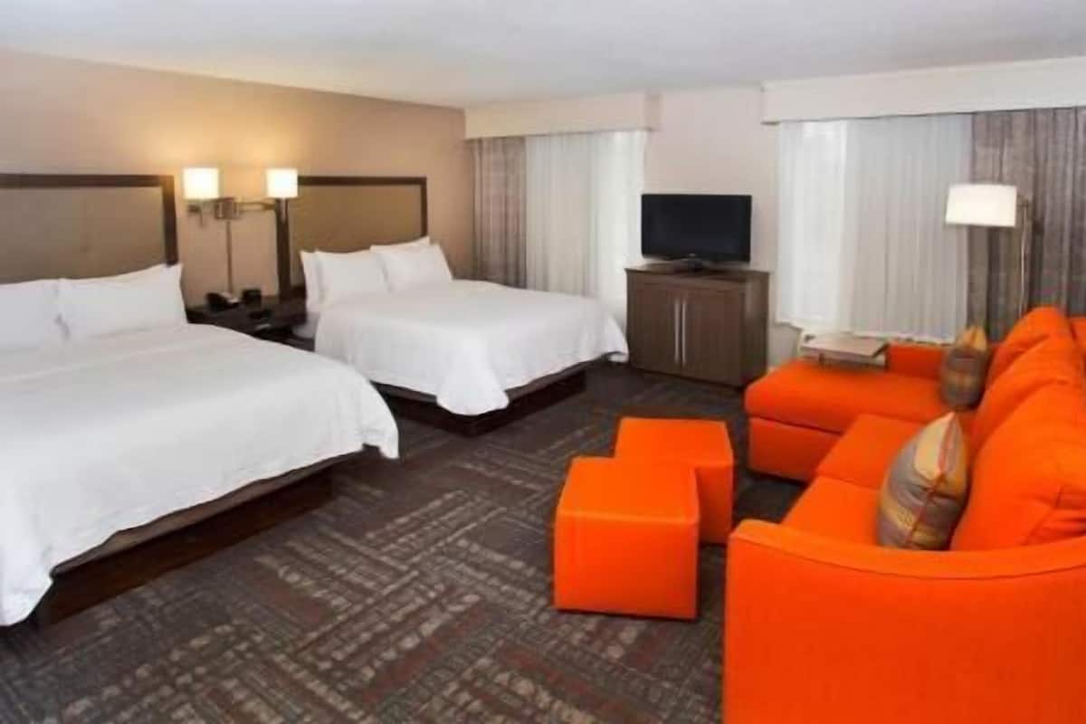 A hotel room with two beds, a television, an orange sofa, and a patterned carpet.