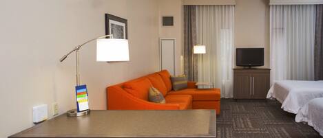 Ett hotellrum med en säng, ett skrivbord, en soffa, en tv och en spegel.