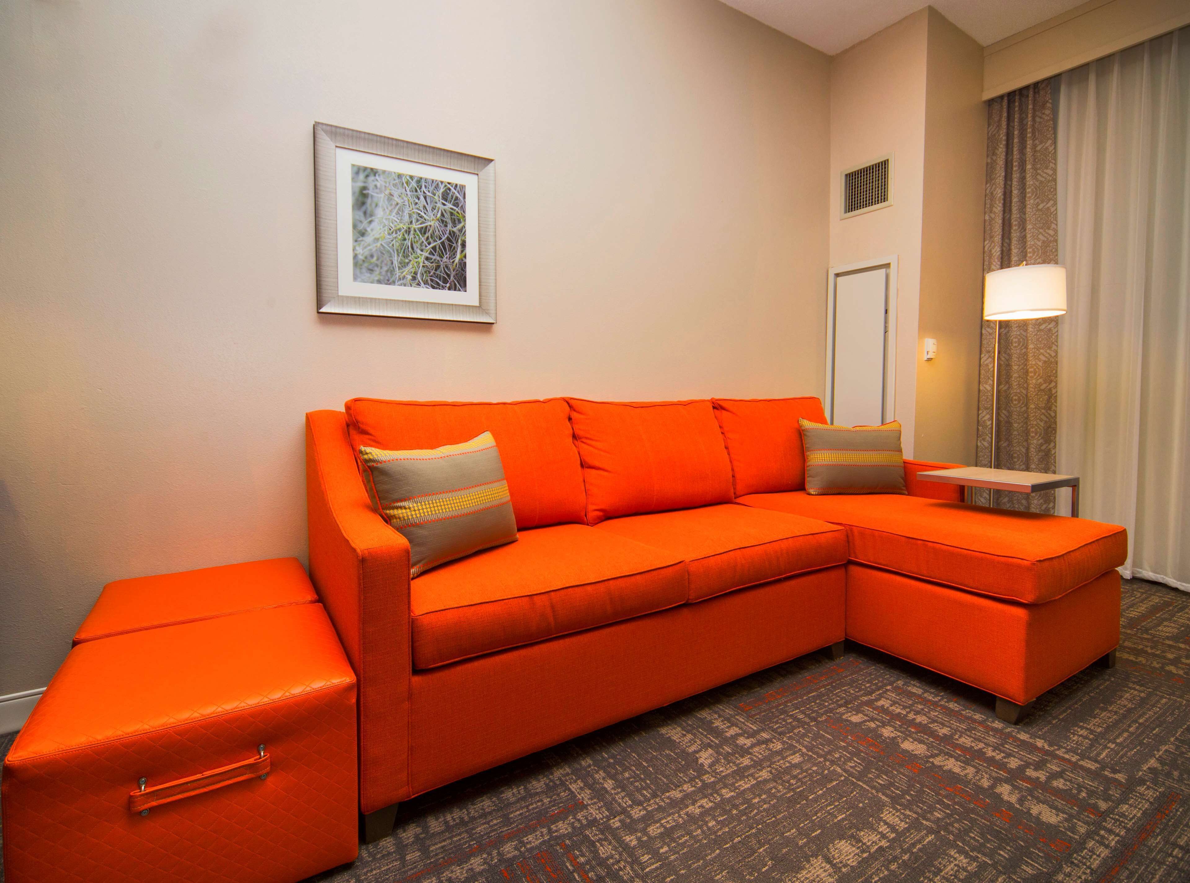 Quarto de hotel moderno com um sofá seccional laranja grande, uma mesinha e uma cama de casal.