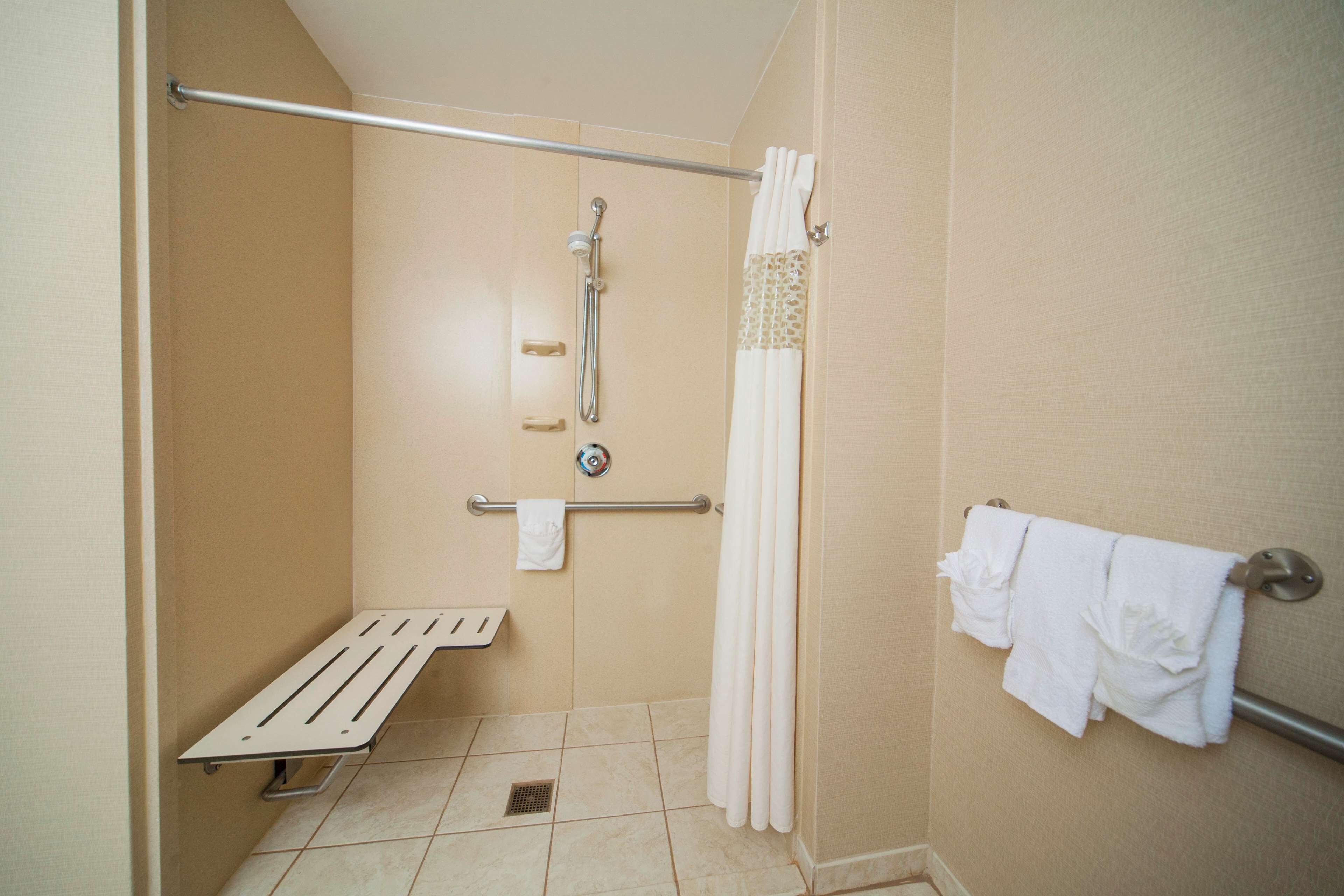 Un petit espace douche fermé, équipé d’une barre d’appui, d’un porte-serviettes blanc et d’un rideau de douche.