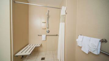 Un petit espace douche fermé, équipé d’une barre d’appui, d’un porte-serviettes blanc et d’un rideau de douche.