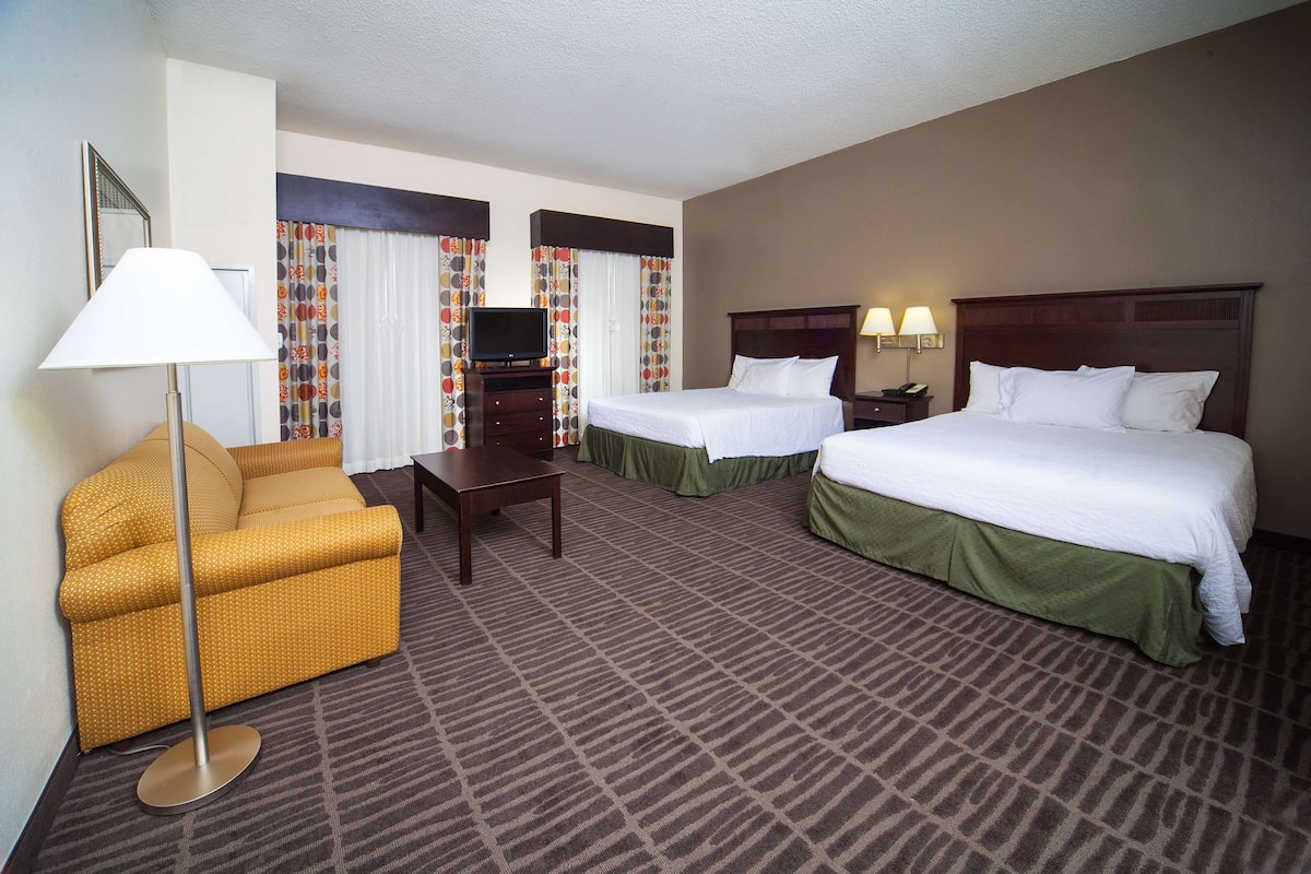 A hotel room with two beds, a sofa, a TV, and a lamp.