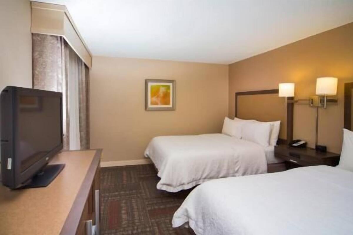 A hotel room with two beds, a television, a painting, and two bedside lamps.