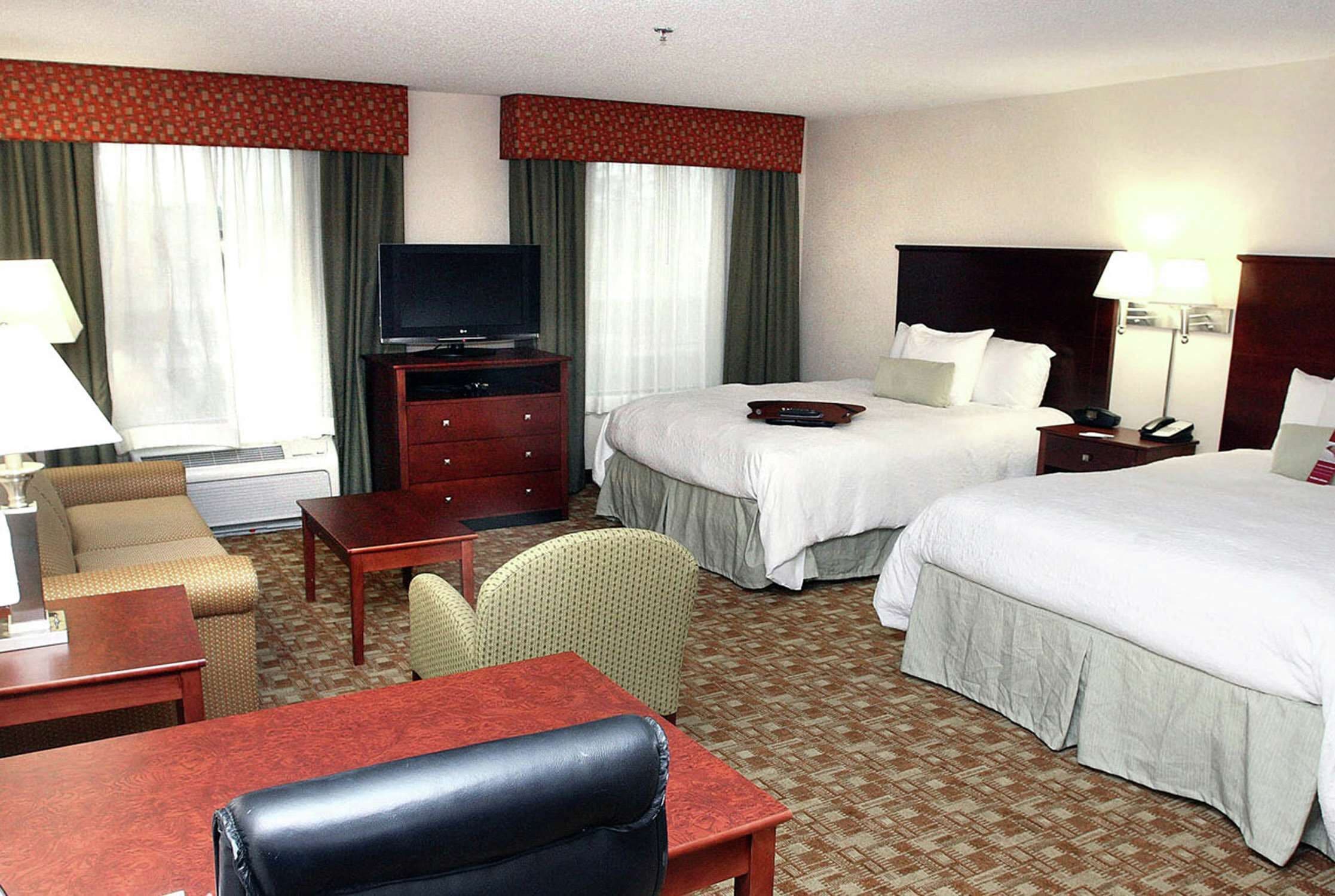 A hotel room with two beds, a television, a desk, a chair, and a lamp.