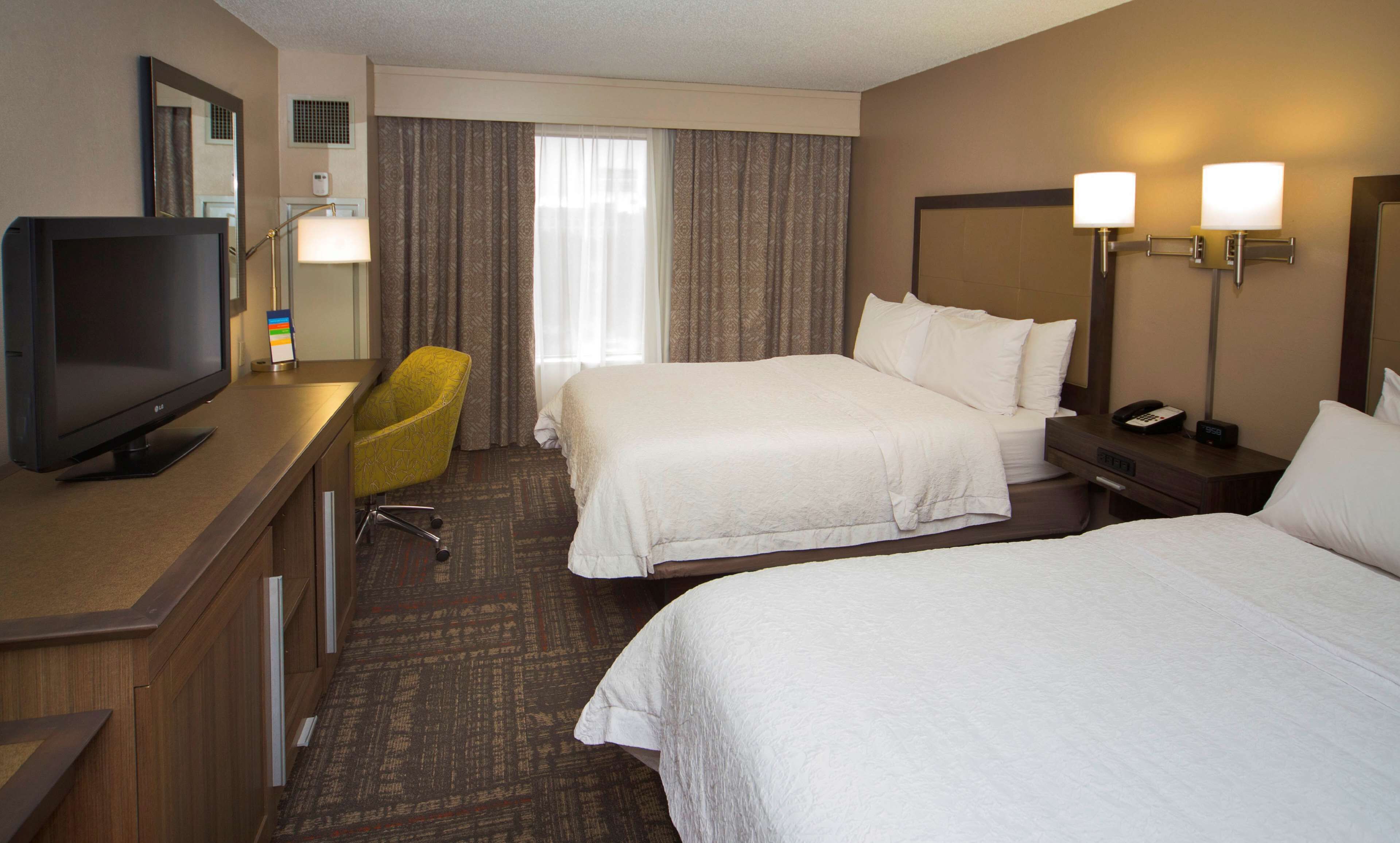 A hotel room with a bed, a desk with a TV, a chair, and two bedside lamps.