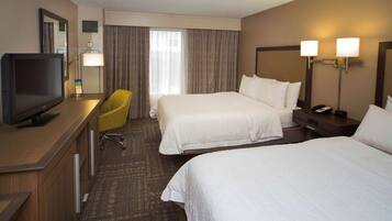 A hotel room with a bed, a desk with a TV, a chair, and two bedside lamps.