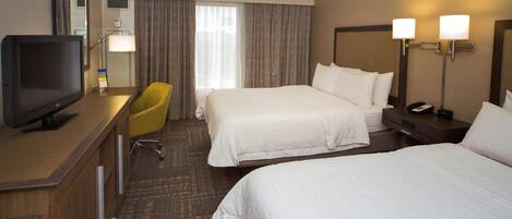 A hotel room with a bed, a desk with a TV, a chair, and two bedside lamps.