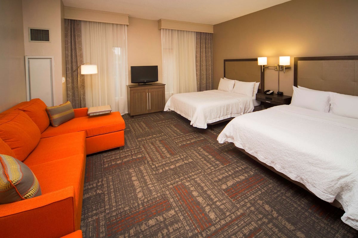 A hotel room with a large bed, a smaller bed, a sofa, a television, and a desk with a lamp.
