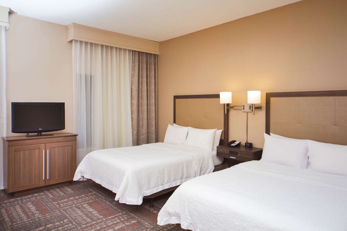 A hotel room with two beds, a television on a wooden cabinet, and a nightstand with a lamp.