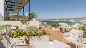 A rooftop terrace with outdoor seating, potted plants, and a view of the coastline.