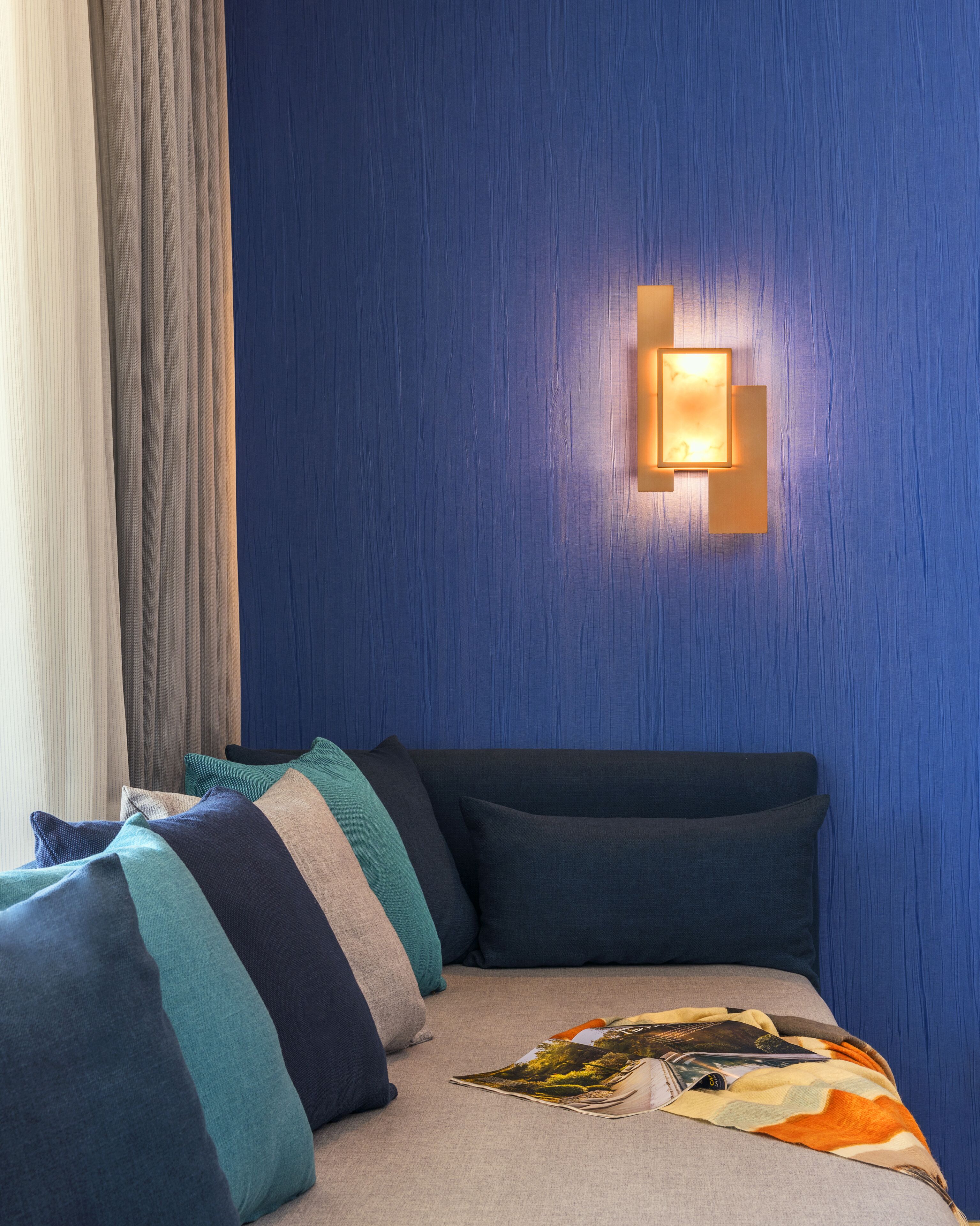 A bedroom with a blue wall, a bed with multiple pillows, and a wall-mounted light fixture.