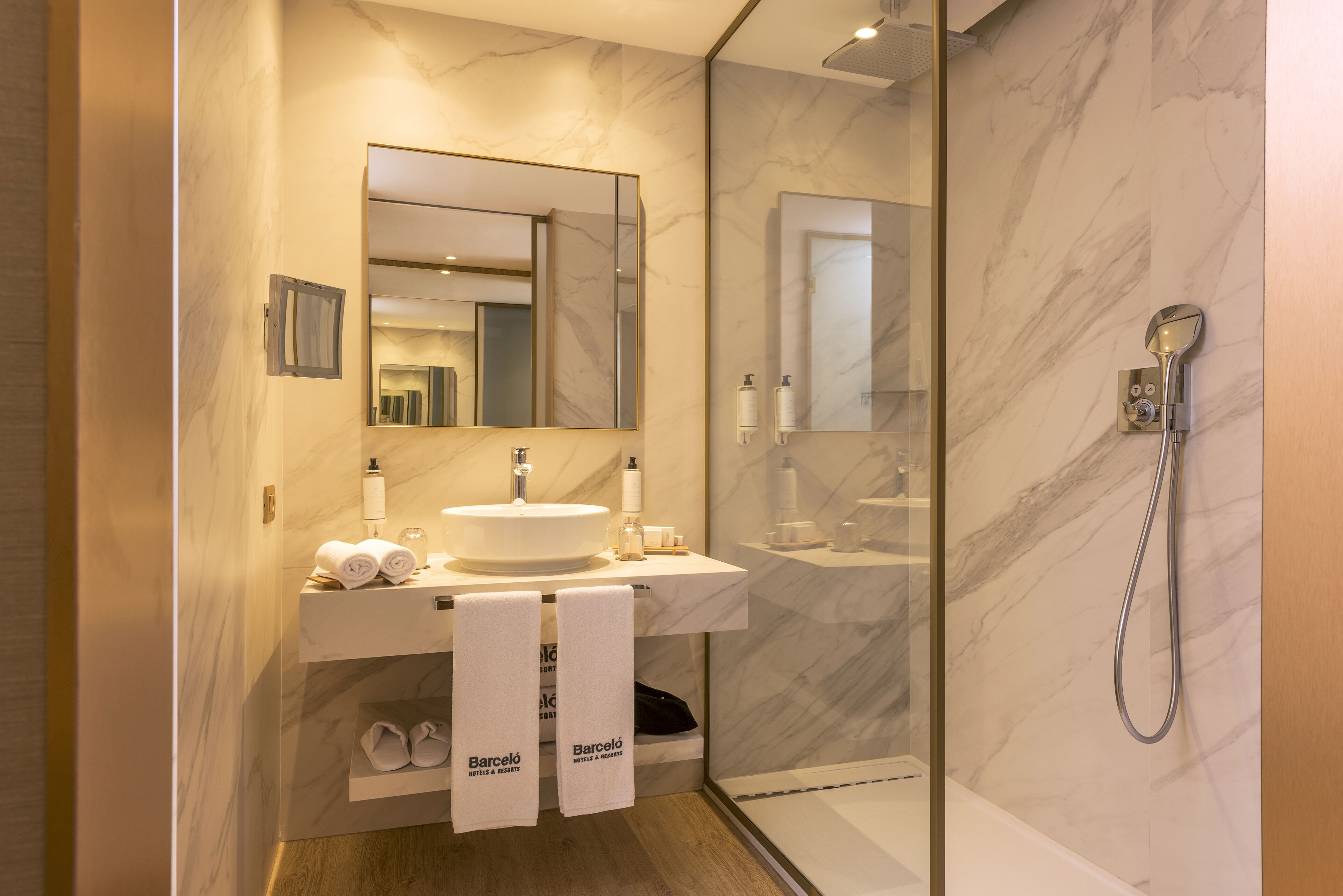 Un baño moderno con lavamanos de mármol, un espejo grande y una zona de ducha con mampara de vidrio.