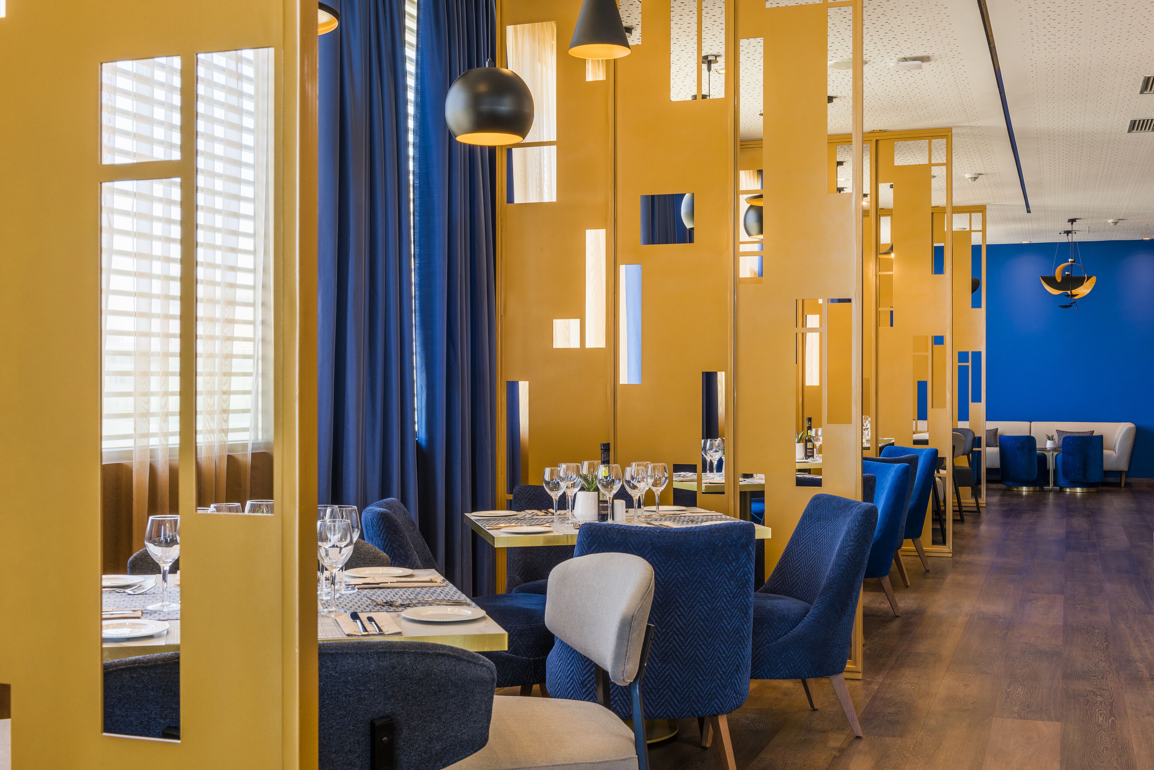 A modern dining area with blue upholstered chairs, yellow walls, and a blue ceiling.