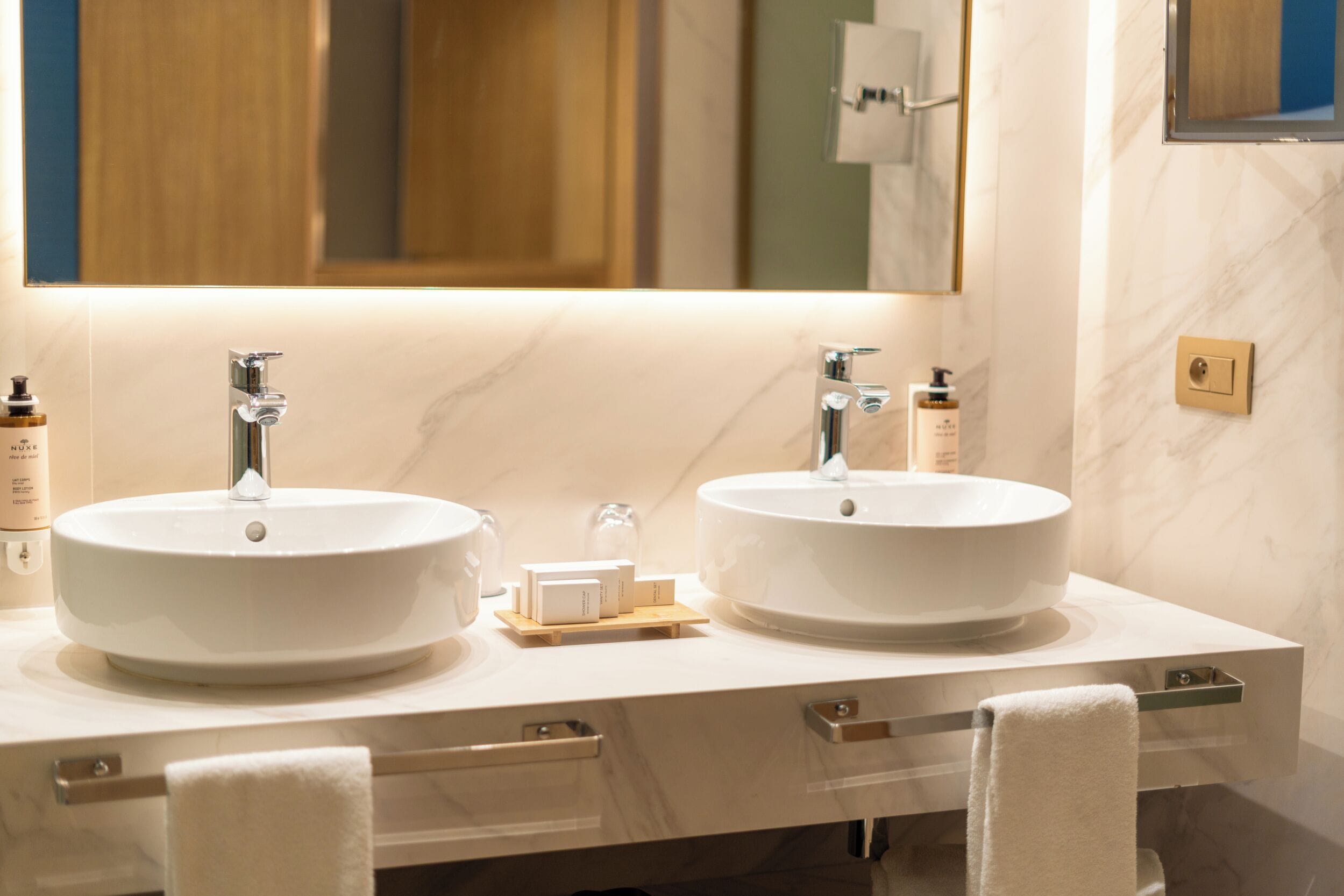 A modern bathroom with two sinks, a mirror, and a towel rack.