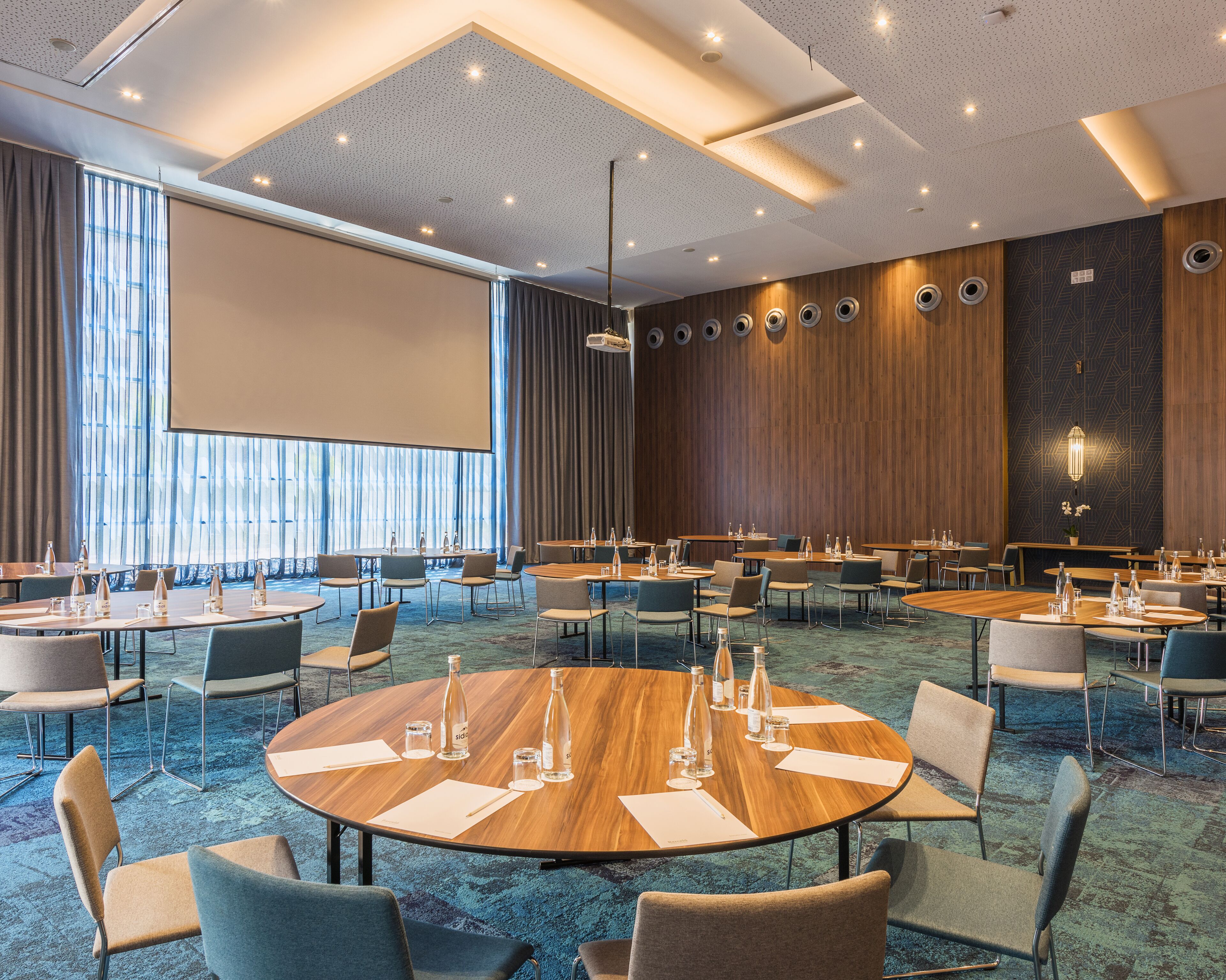 A conference room with round tables, chairs, and a large screen.