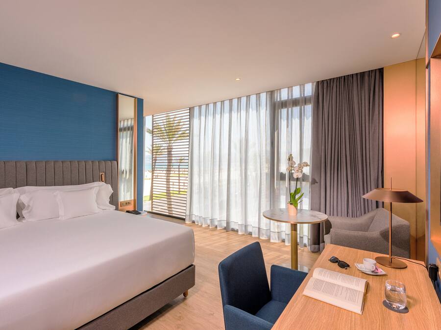 A modern hotel room with a large bed, a desk with a chair, a small table, and a TV.