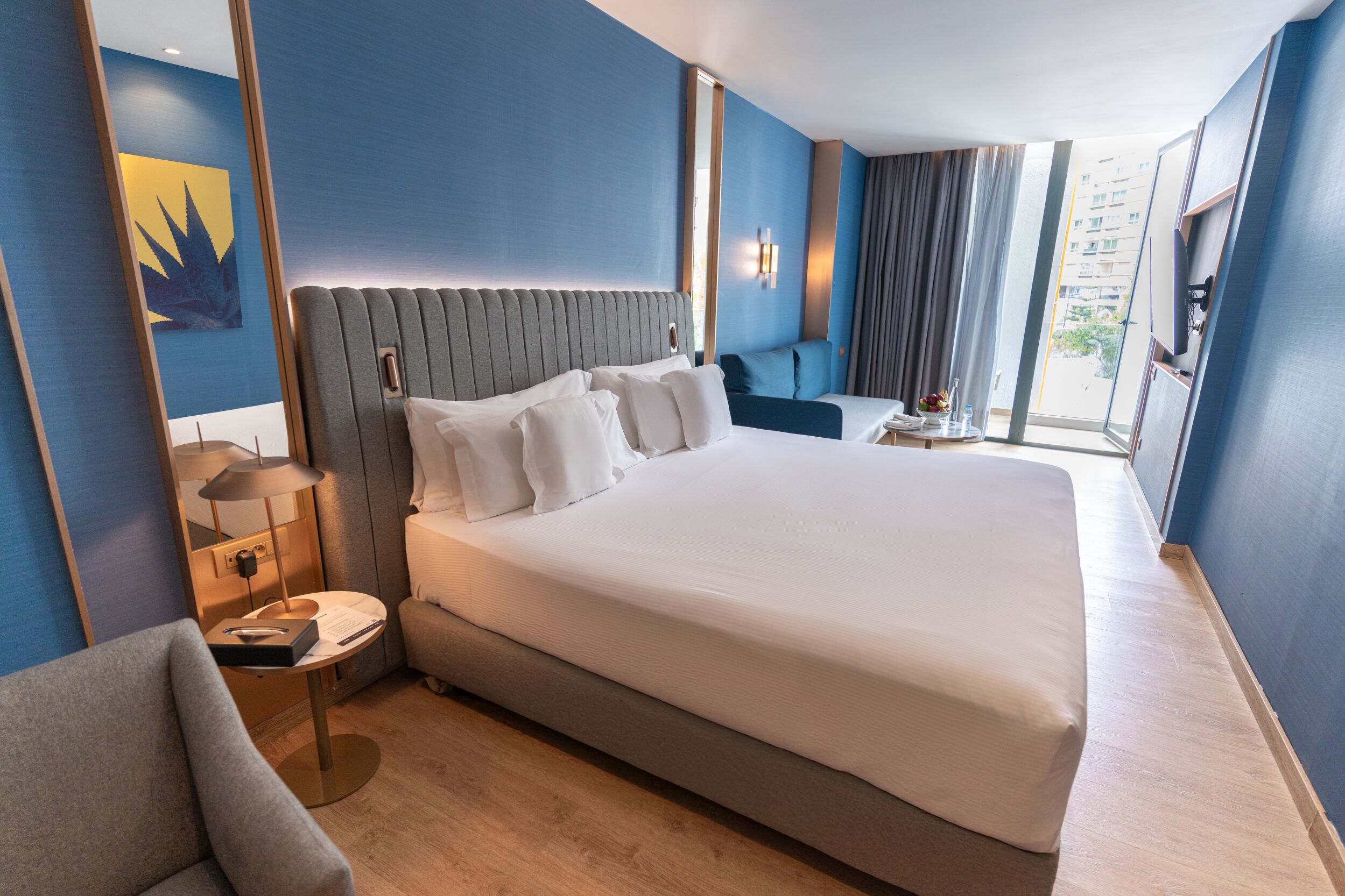 Habitación de hotel con una cama grande, un escritorio con lámpara, una silla y vistas a la ciudad.