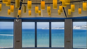 A room with large windows overlooking a beach, featuring hanging yellow pendant lights and a view of the sea.