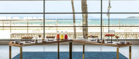 Une pièce dotée d’une grande fenêtre donnant sur une plage, une table sur laquelle sont disposés divers aliments et un tapis bleu.