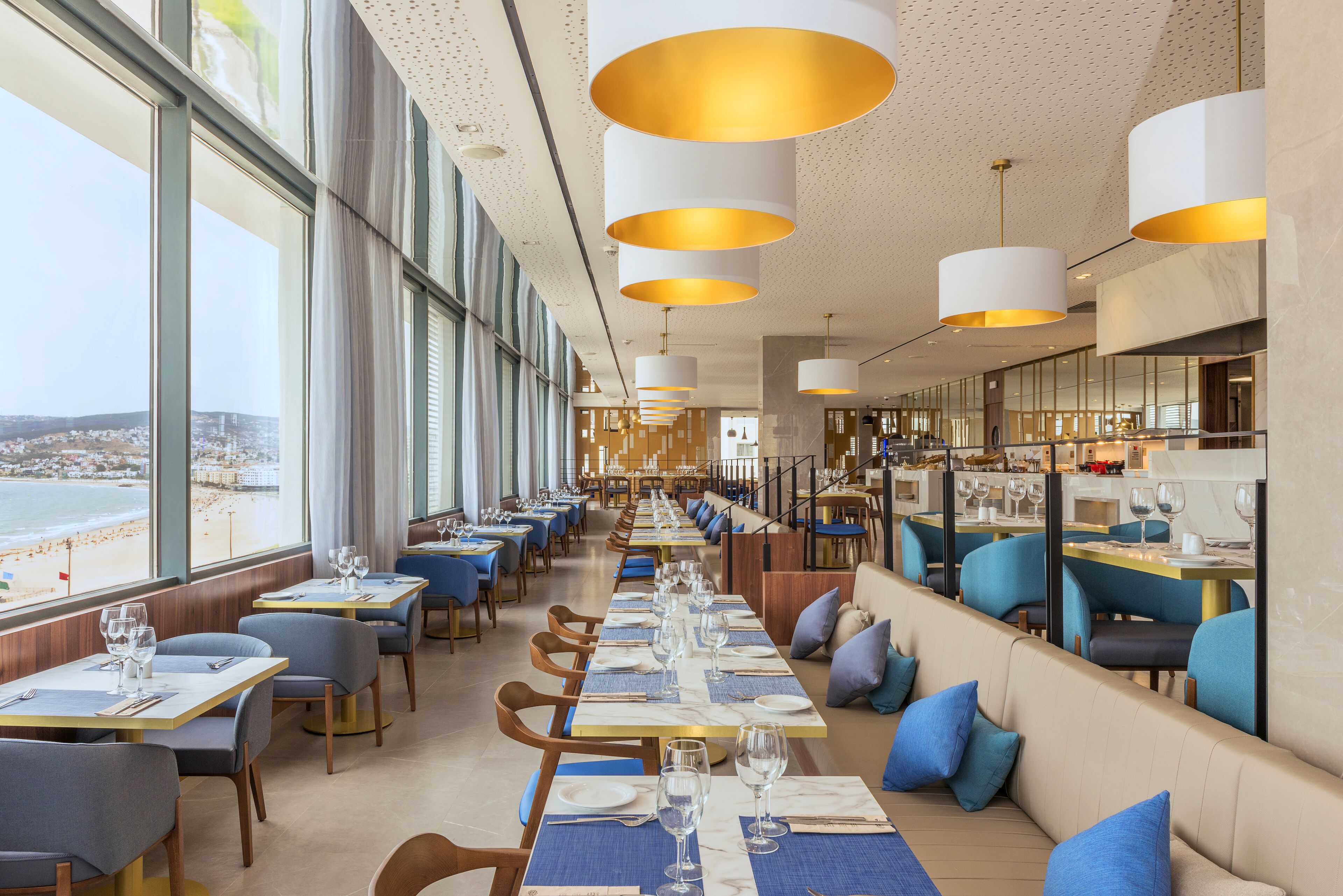A long dining area with tables set for a meal, overlooking a beach.