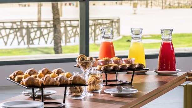 A breakfast buffet with pastries and drinks, overlooking a beach and ocean view.