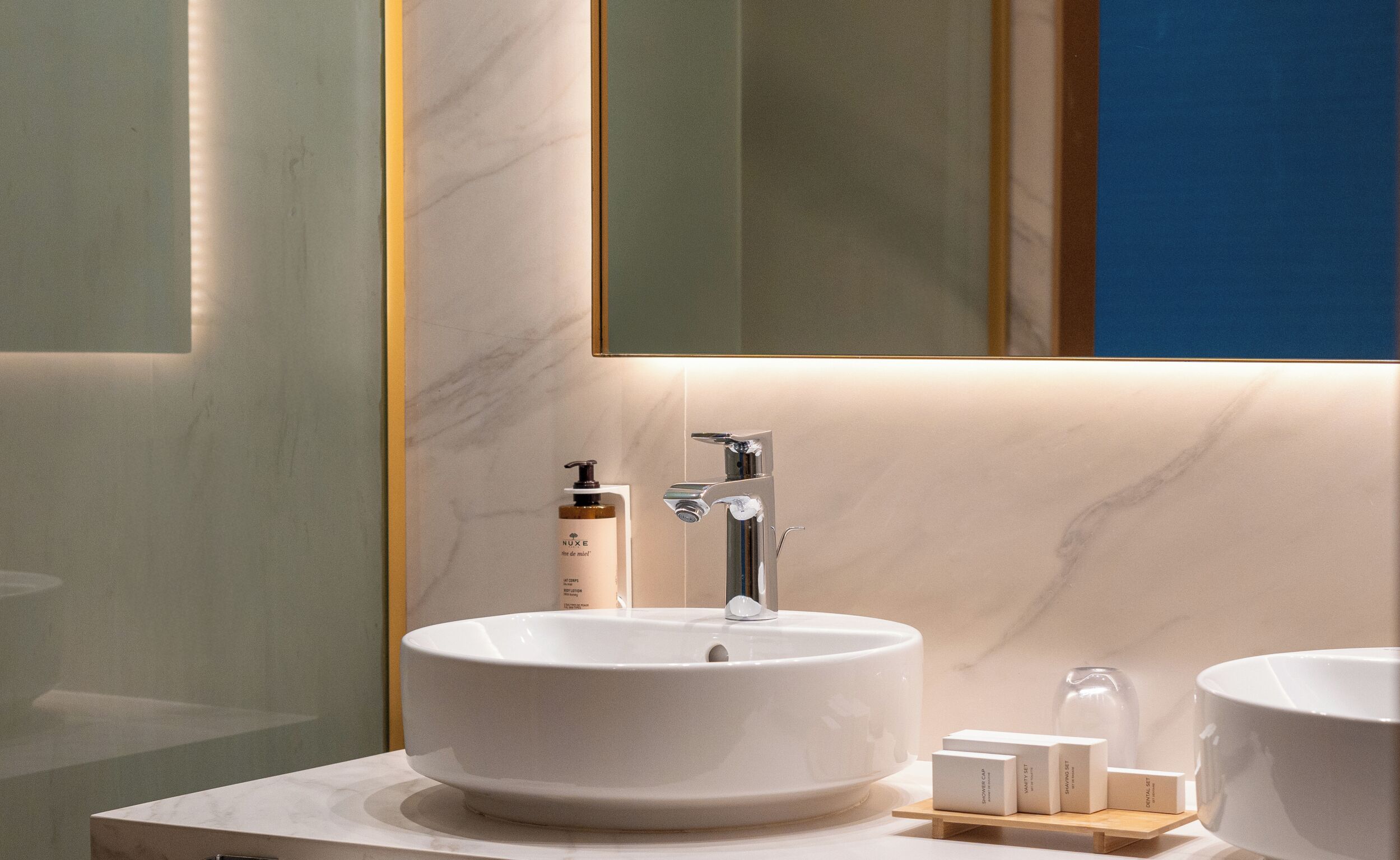 Une salle de bain avec un grand lavabo blanc, un miroir et une bouteille de shampoing.