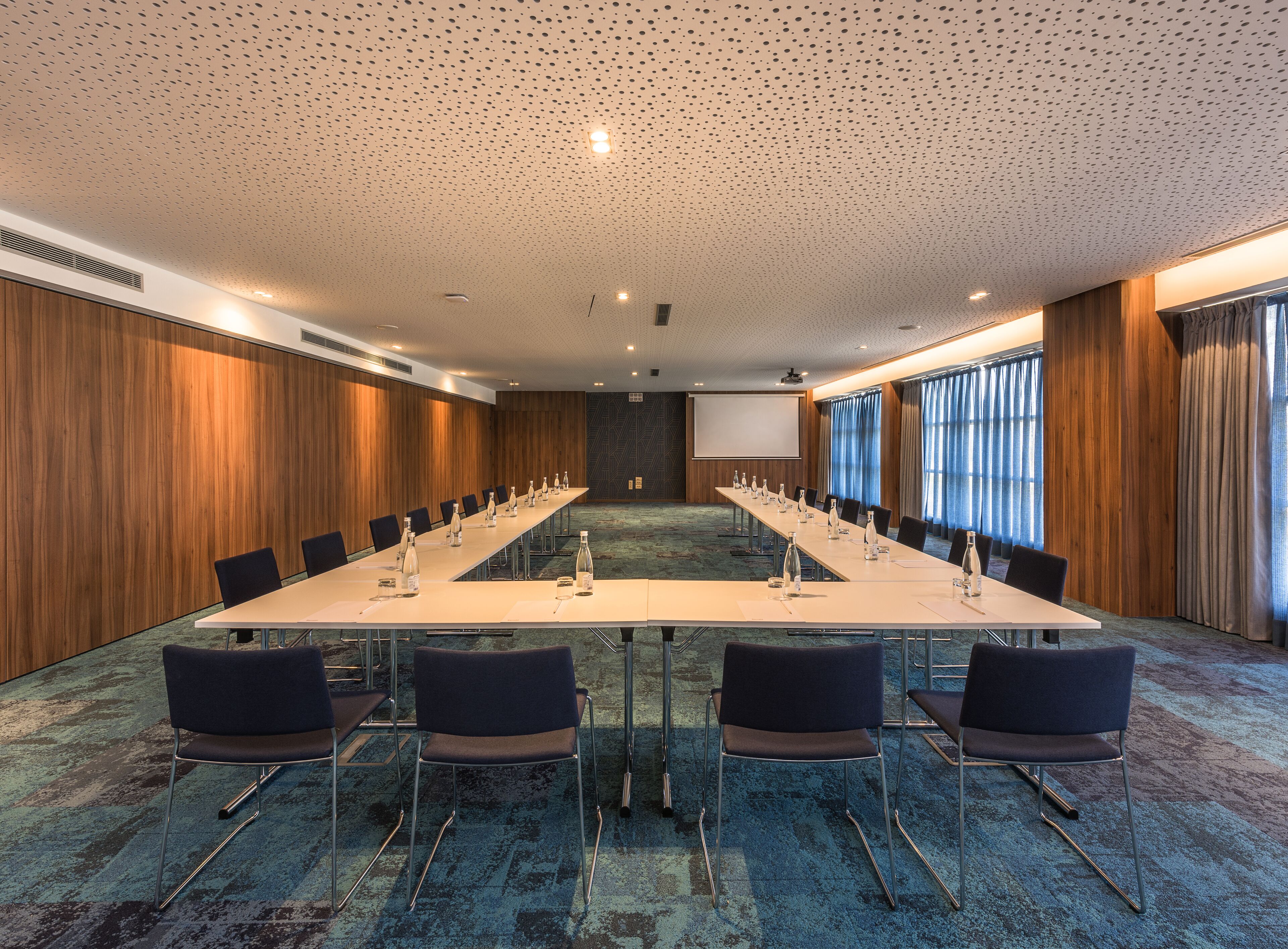 A conference room with a long table, chairs, a projector screen, and a carpeted floor.