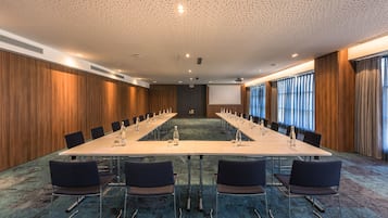 A conference room with a long table, chairs, a projector screen, and a carpeted floor.