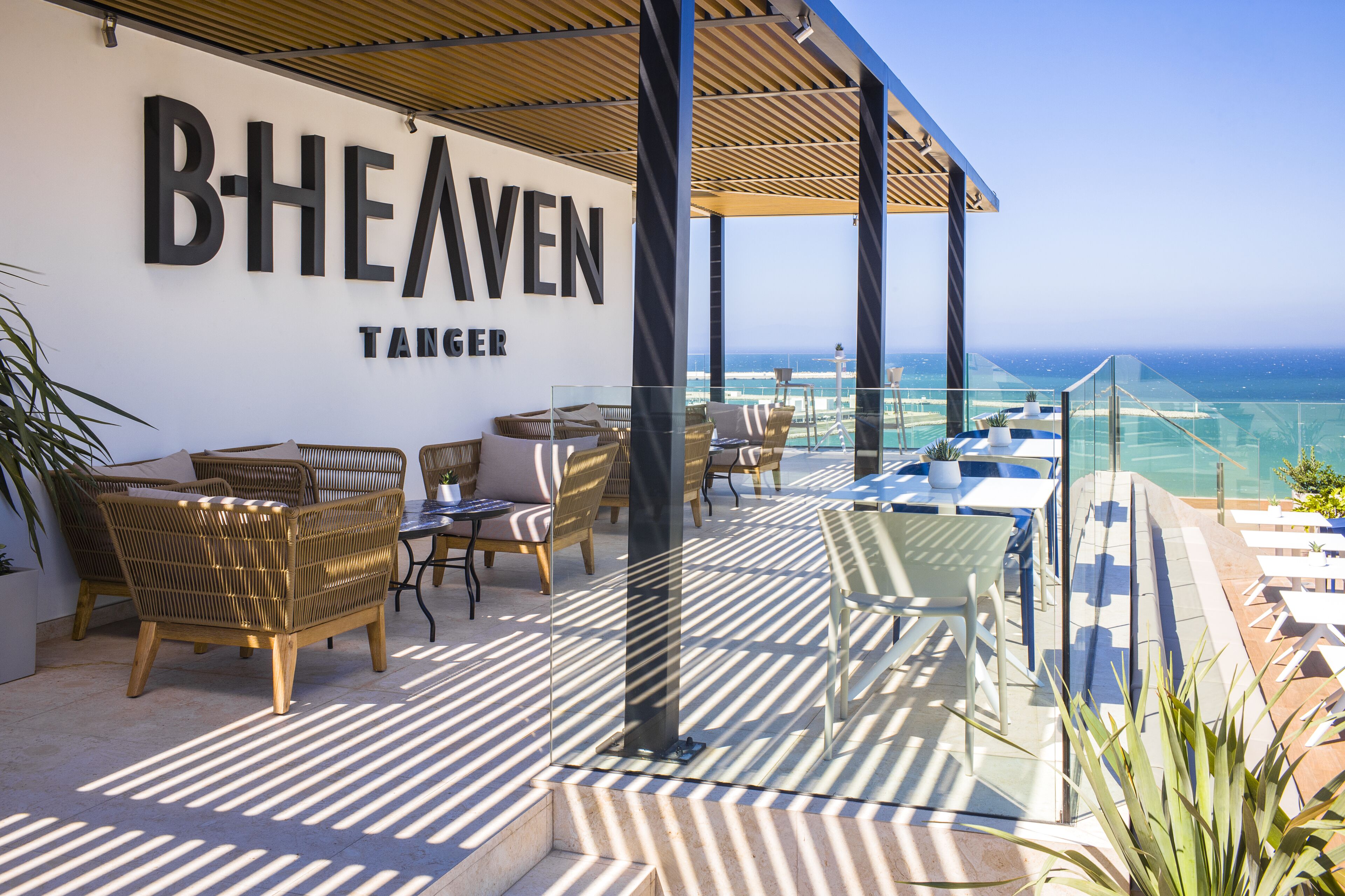 A rooftop terrace with wicker furniture, a glass balustrade, and a view of the ocean.