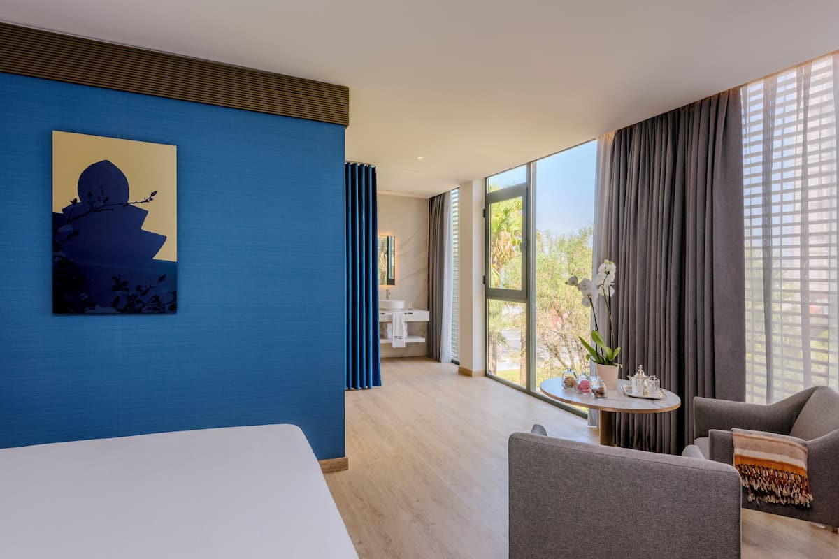 A modern hotel room with a large window, a painting on the wall, and a view of the outdoors.