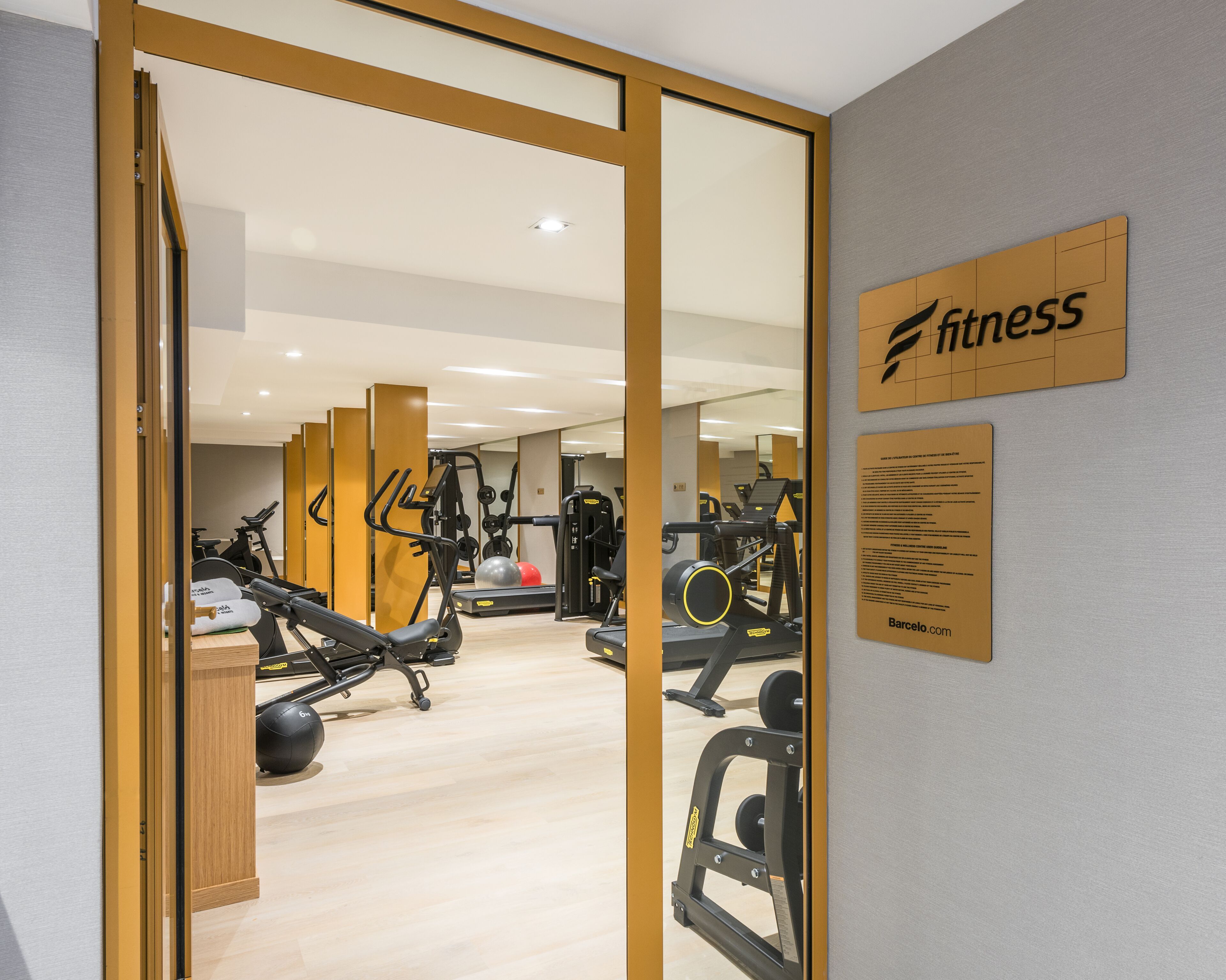 A gym with exercise equipment, a wooden floor, and a sign that says "fitness".