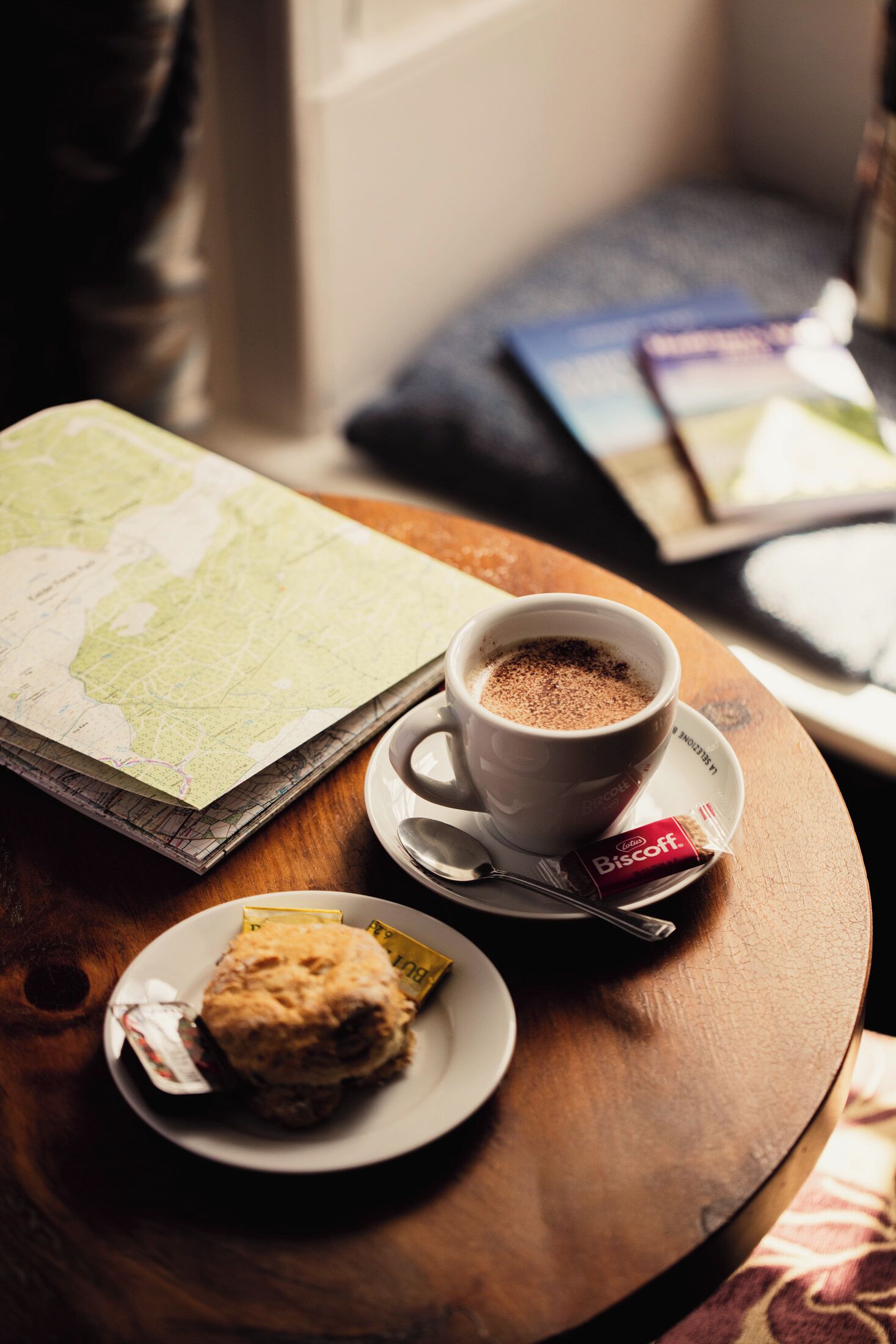 A table with a cup of coffee, a biscuit, a map, and a book.