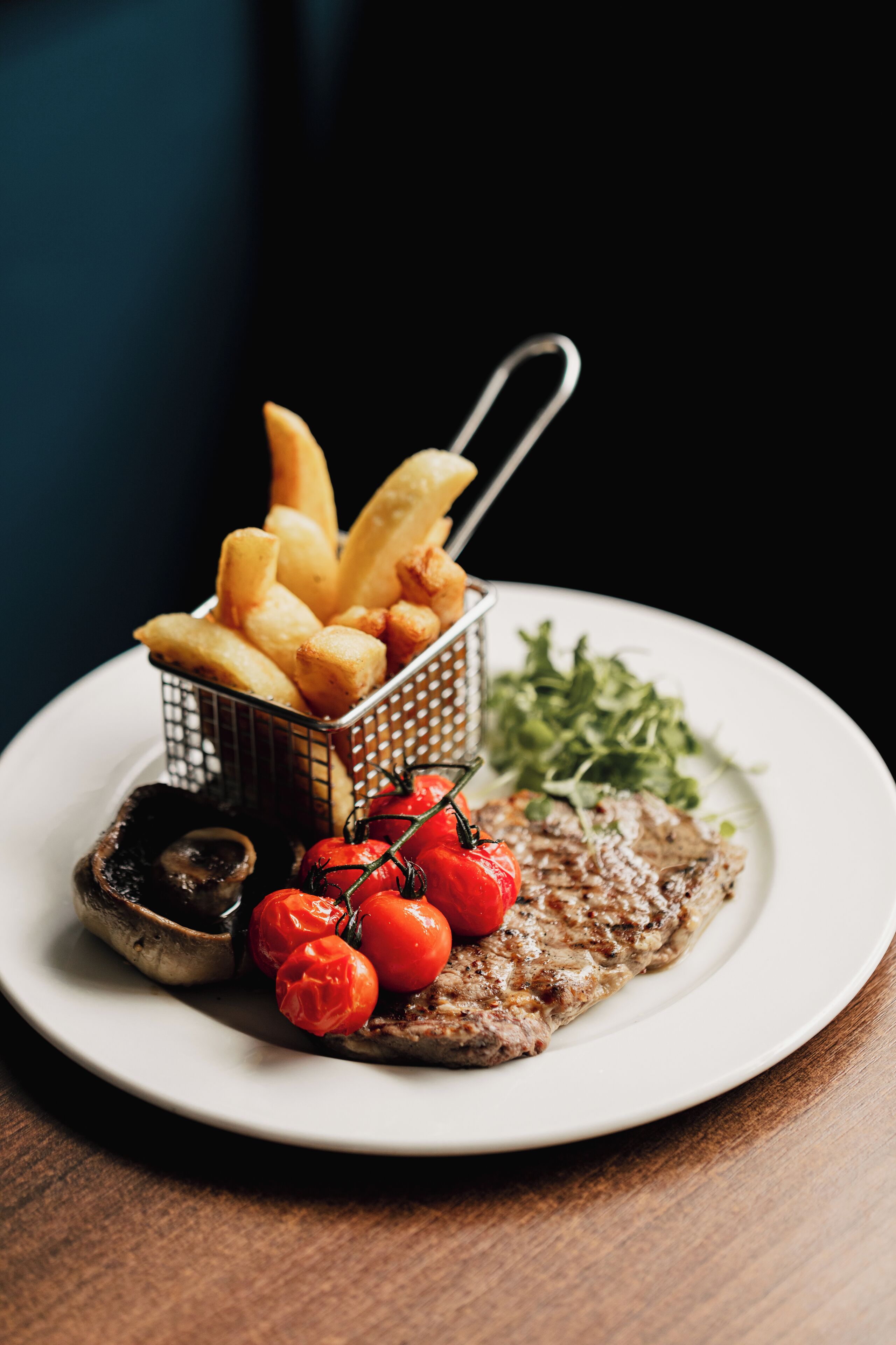 A plate with a steak, cherry tomatoes, a side salad, and French fries.