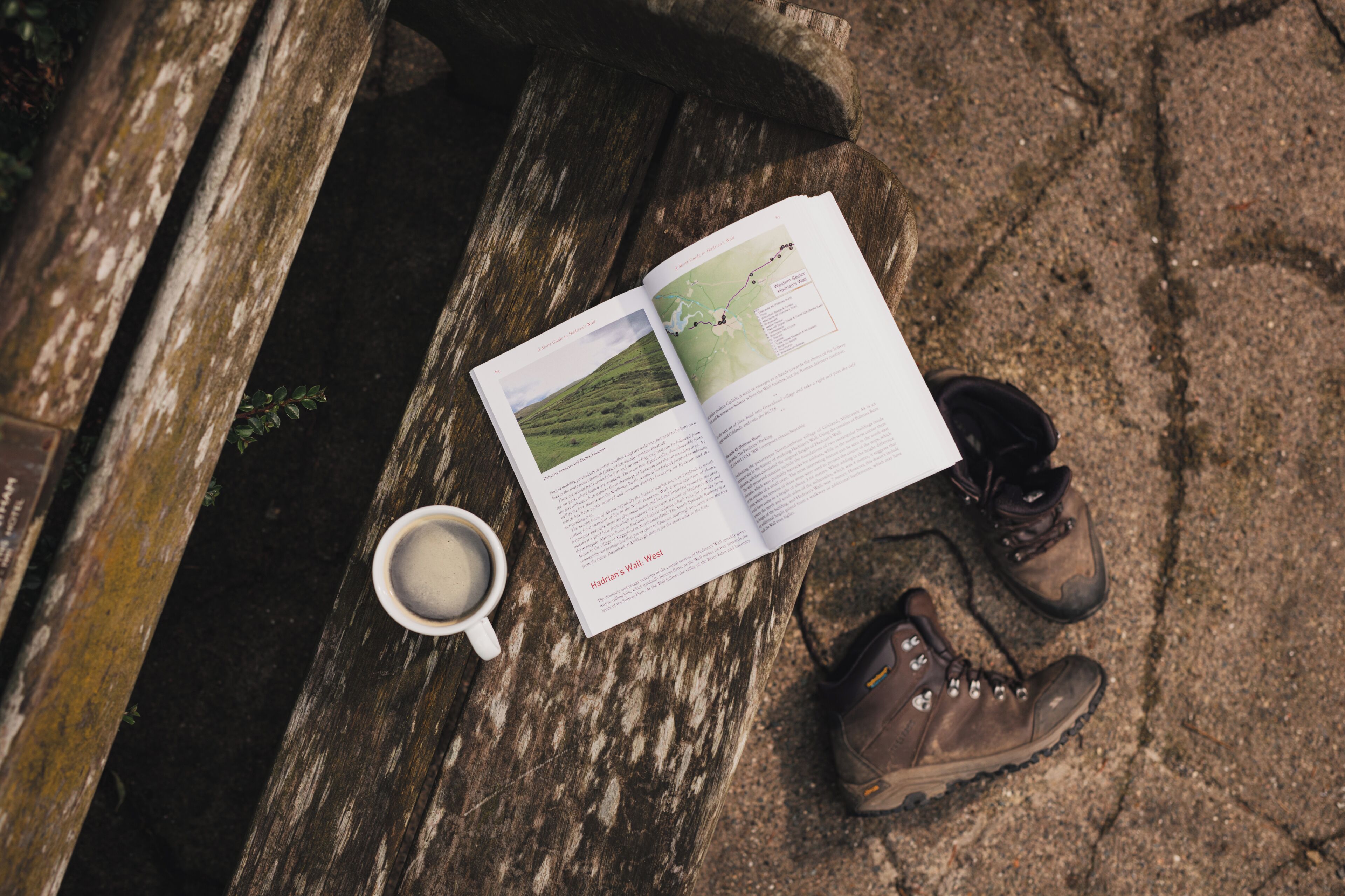 A book, a cup, and a pair of boots on a wooden bench.