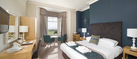 A hotel room with a large bed, a desk with a telephone, a chair, a nightstand, and a window with curtains.