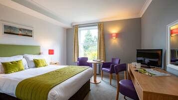 Ein Hotelzimmer mit Bett, Schreibtisch, Stuhl, Fernseher und einem Fenster mit Vorhängen.