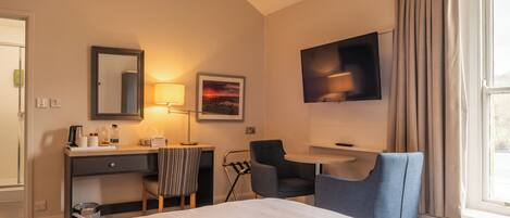 A hotel room with a bed, desk, chair, TV, and a window with curtains.