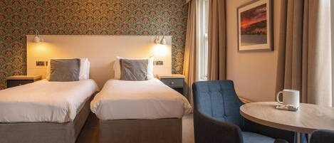 A hotel room with two beds, a small table, and a chair.