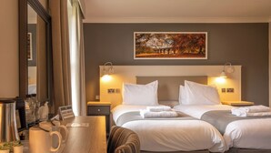 Una habitación de hotel con dos camas, un escritorio con cafetera, un espejo y un cuadro en la pared.