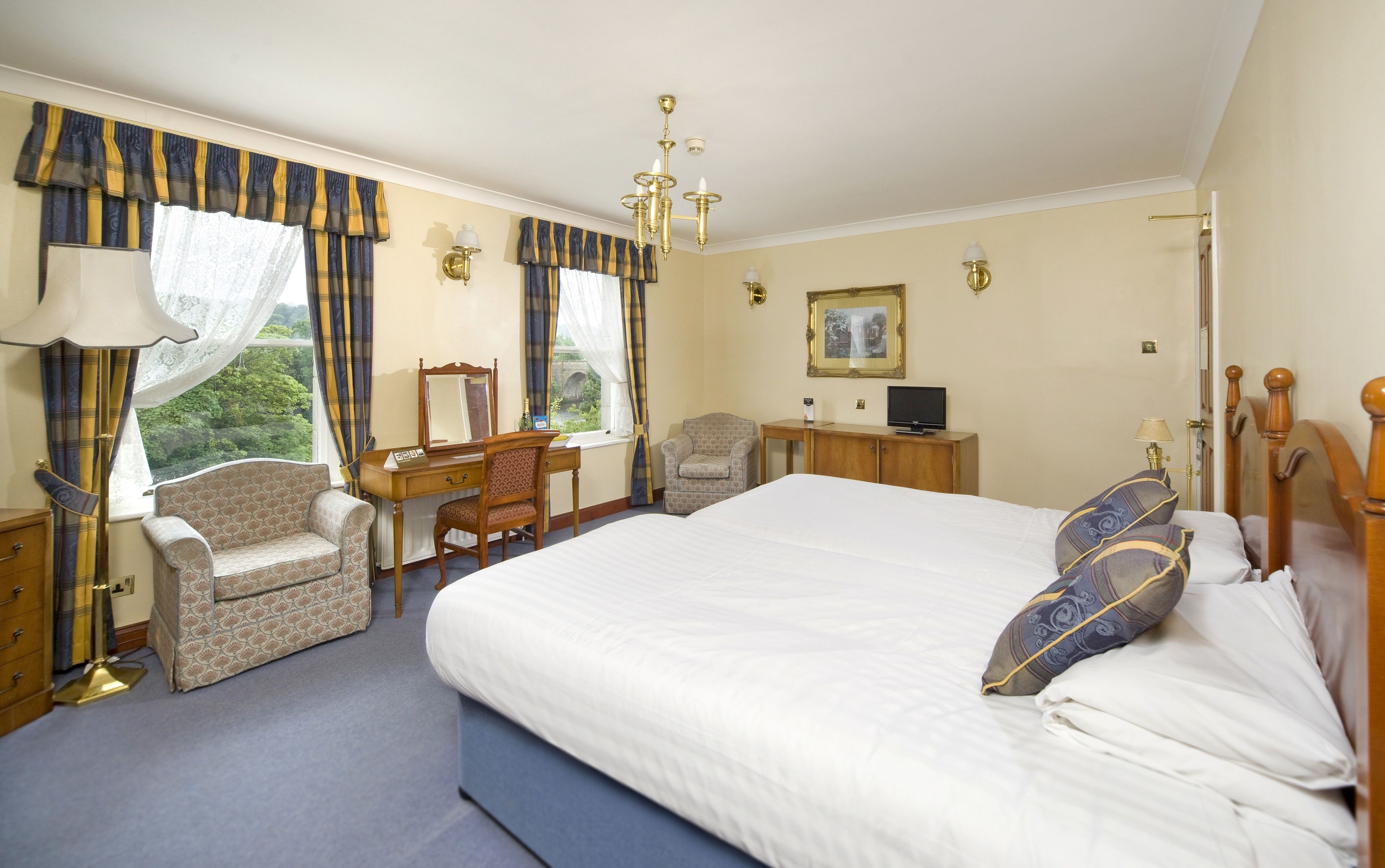 A hotel room with a large bed, a desk with a chair, a television, and a window with curtains.