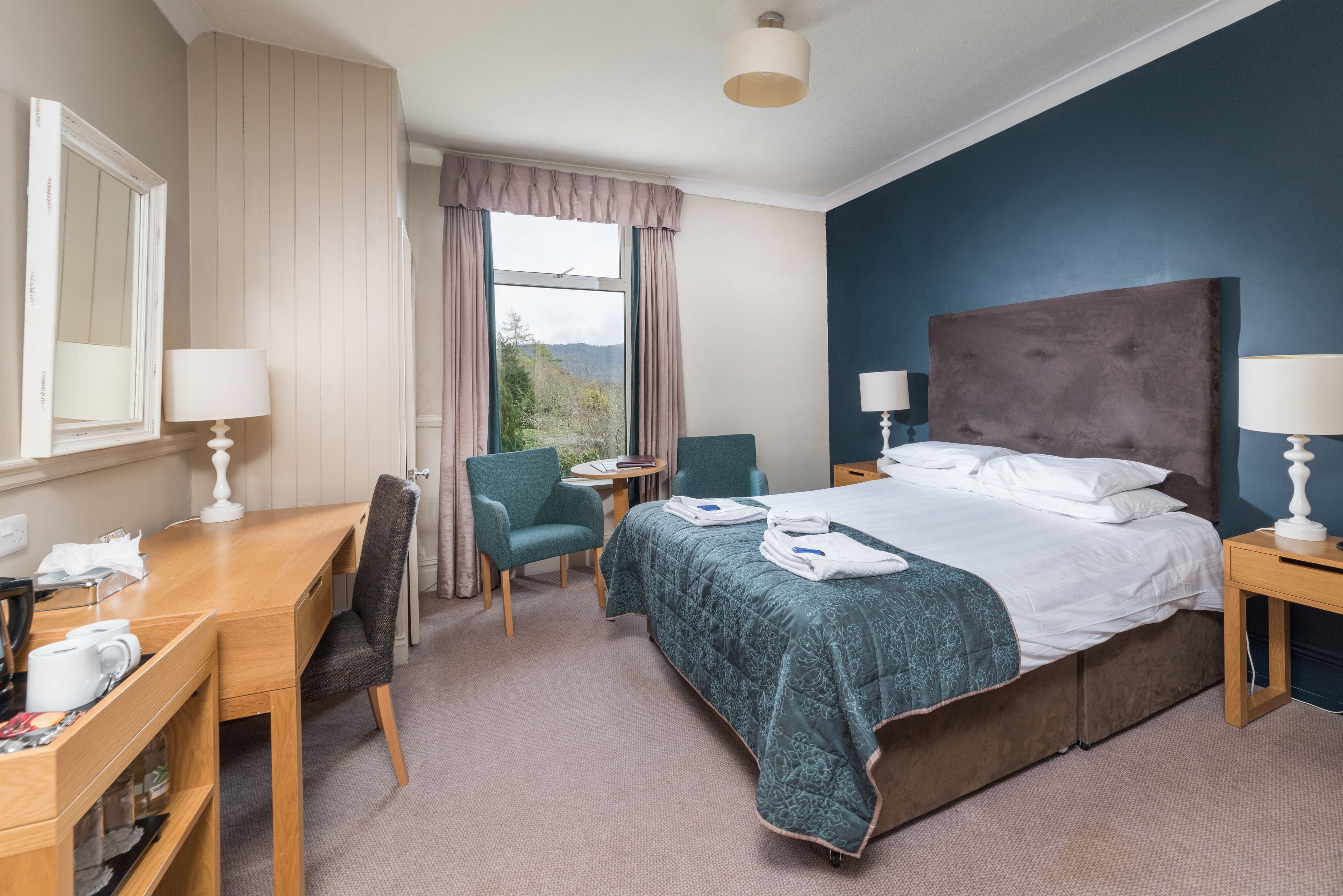 A hotel room with a bed, desk, chairs, and a window with curtains.
