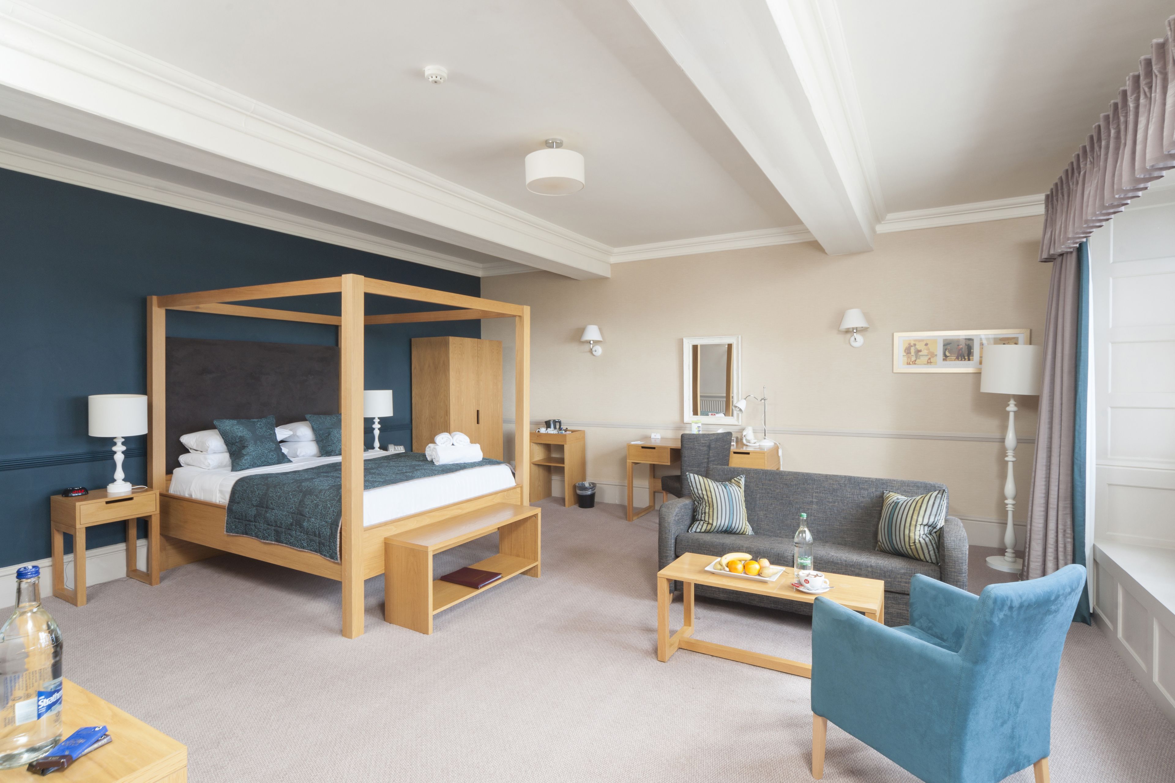 A hotel room with a four-poster bed, a sofa, a coffee table, and a small desk.