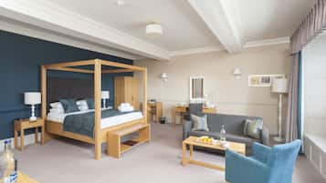 A hotel room with a four-poster bed, a sofa, a coffee table, and a small desk.