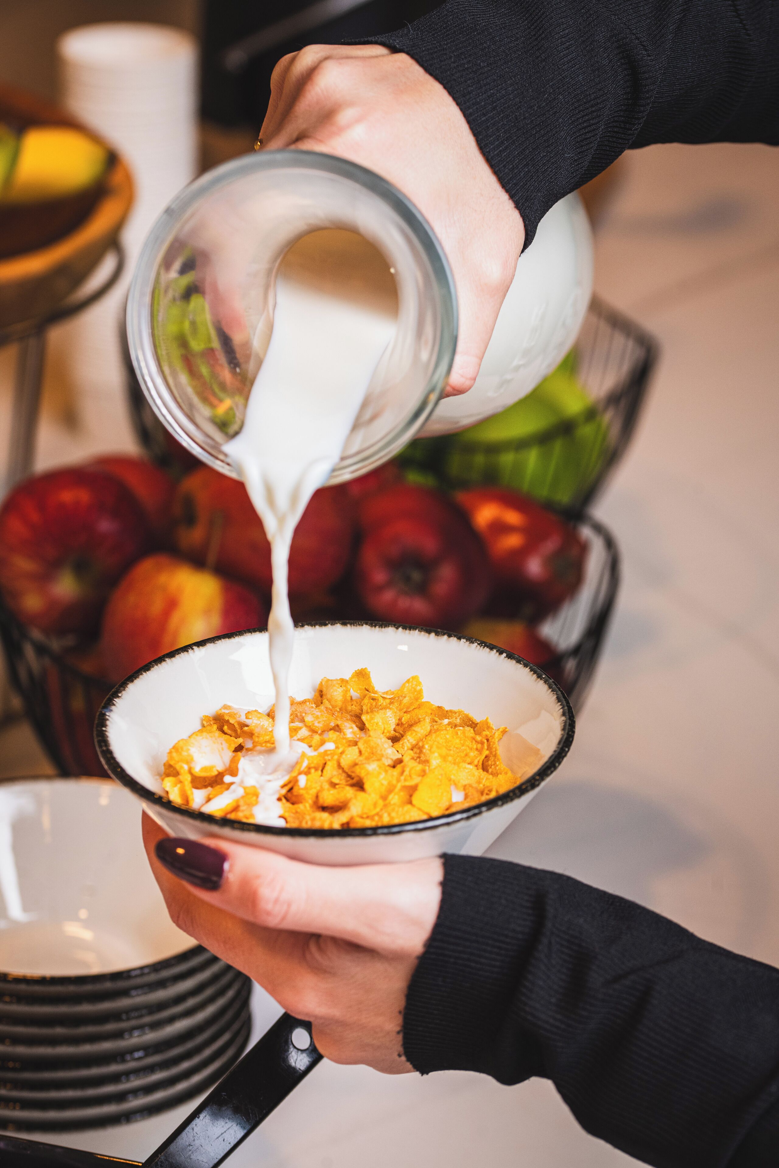 A person pouring milk into a bowl of cereal.