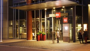 Una entrada de hotel moderna con fachada de vidrio, una columna vertical destacada y un cartel que dice "ibis London Excel".