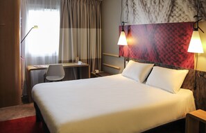 Une chambre d’hôtel avec un grand lit, un bureau avec une chaise, une lampe et un mur au décor texturé.