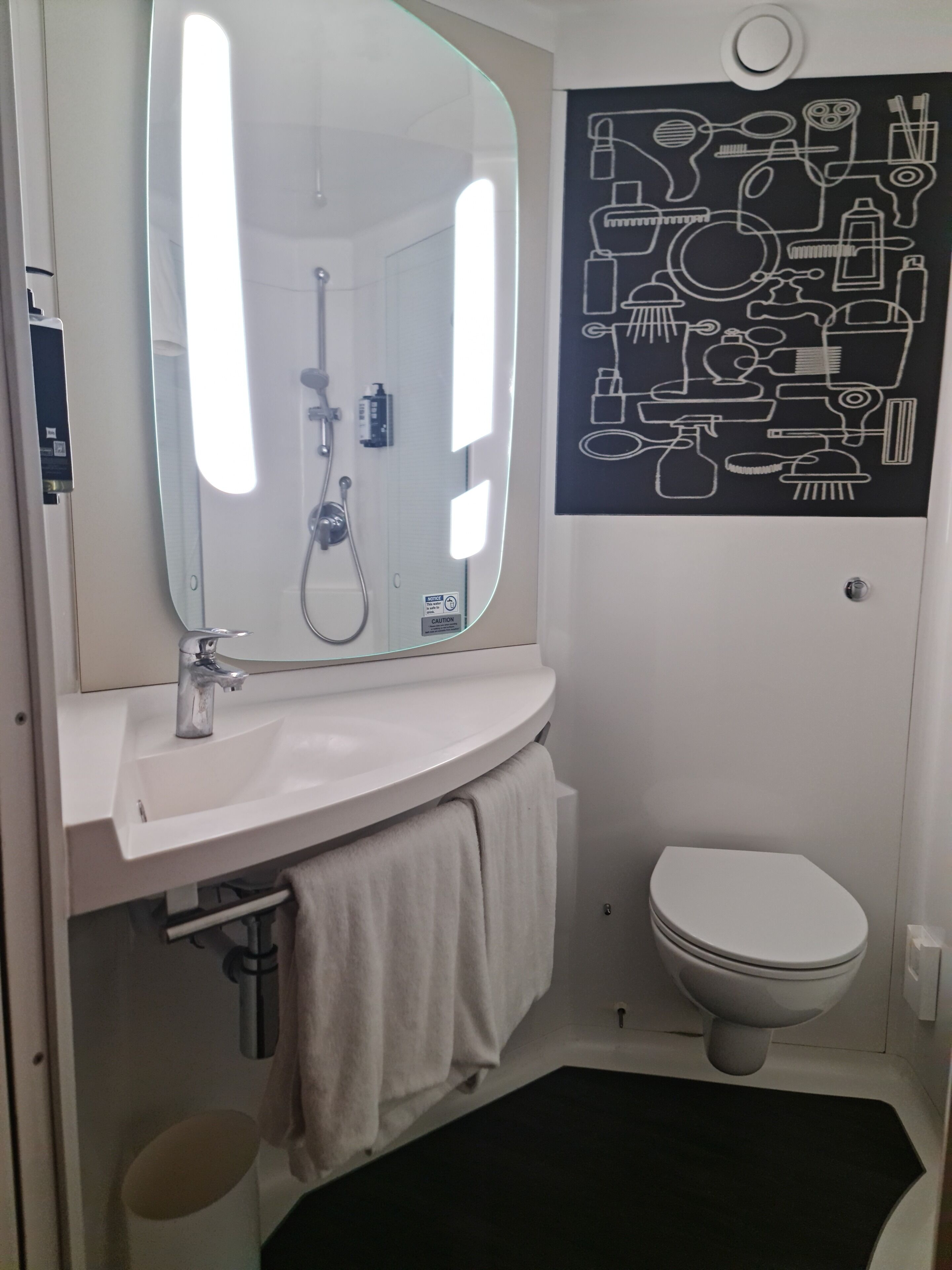 A bathroom with a white sink, a mirror, a toilet, and a black and white bathroom art piece.