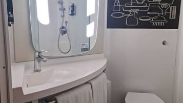 A bathroom with a white sink, a mirror, a toilet, and a black and white bathroom art piece.