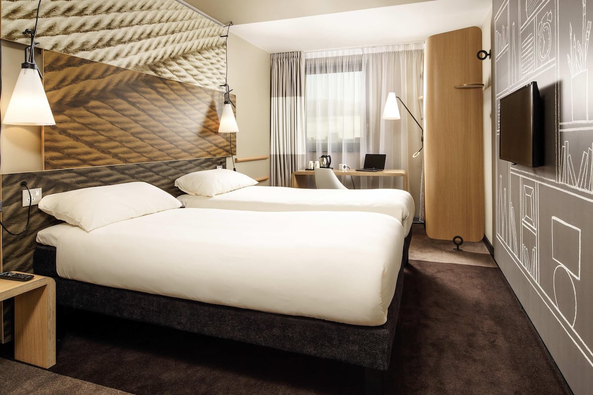 Ett hotellrum med två sängar, ett skrivbord med en bärbar dator, en TV och en vägg med ett mönster.